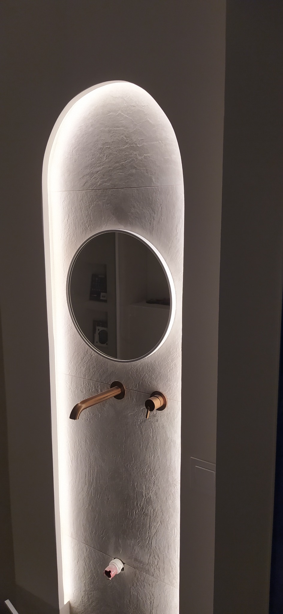 Nowoczesna umywalka z okrągłym lustrem i podświetleniem LED, wykończona w odcieniach szarości i miedzi. Minimalistyczny design z widoczną instalacją hydrauliczną.