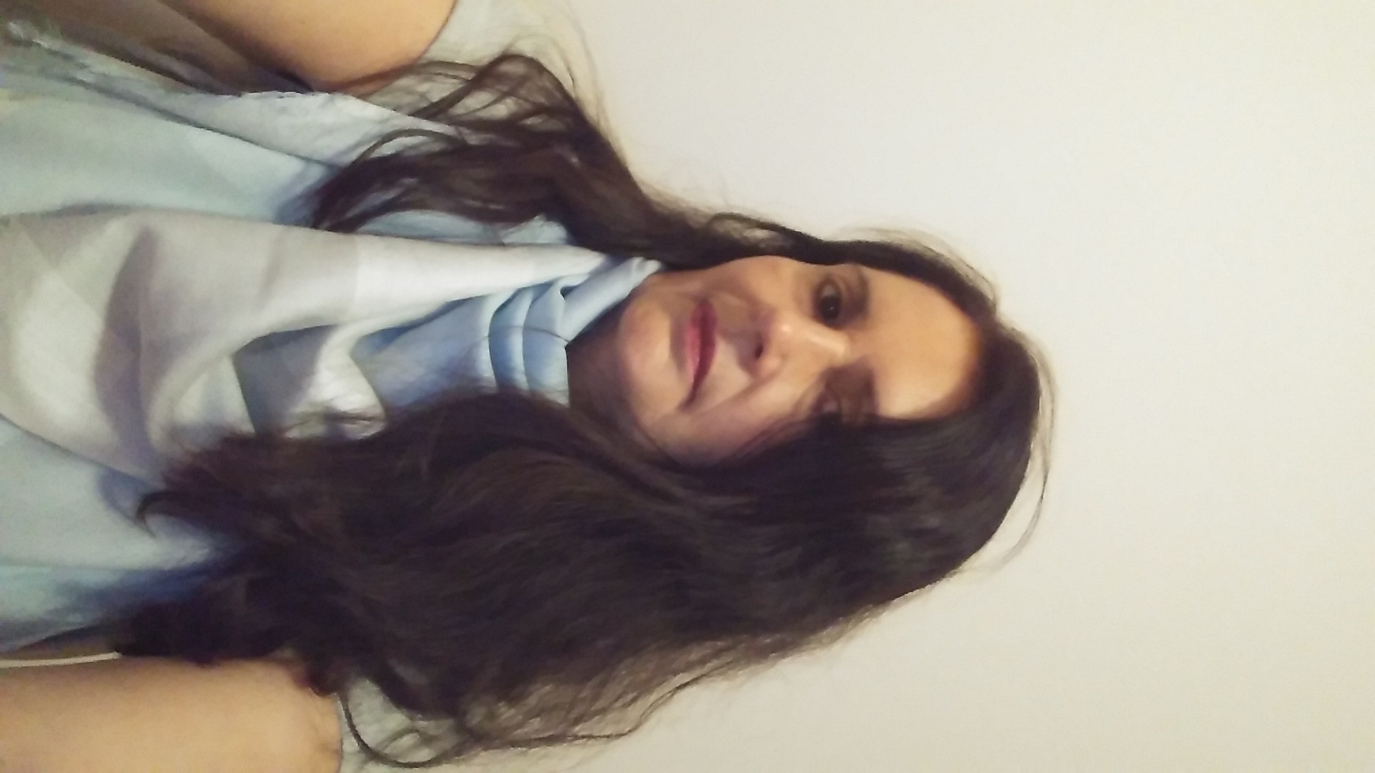 Portret kobiety z długimi, ciemnymi włosami, ubrana w jasnoniebieską bluzkę, sfotografowana z nietypowej perspektywy, z bliska