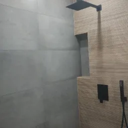 Nowoczesna kabina prysznicowa z szarymi płytami wielkoformatowymi i drewnopodobną ścianą z wnęką, wyposażona w czarną deszczownicę i baterię podtynkową.