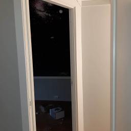 Lukmar - Biała ościeżnica drzwiowa w trakcie montażu, widoczna ściana z motywem kosmosu i porozrzucane elementy montażowe na podłodze.