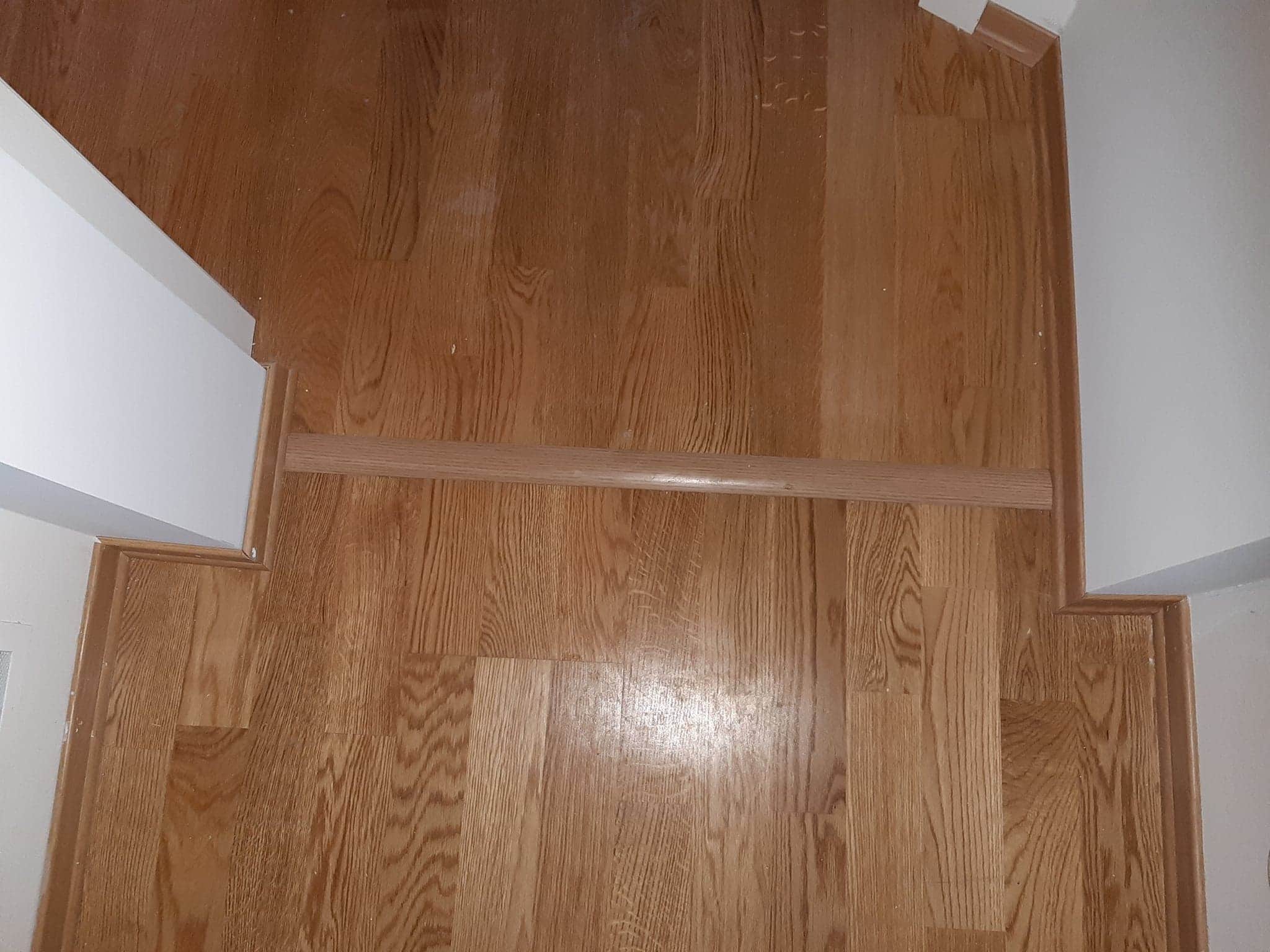 Ułożone panele podłogowe z drewnopodobnym wzorem, widoczny próg łączący pomieszczenia i listwa przypodłogowa przy ścianie.