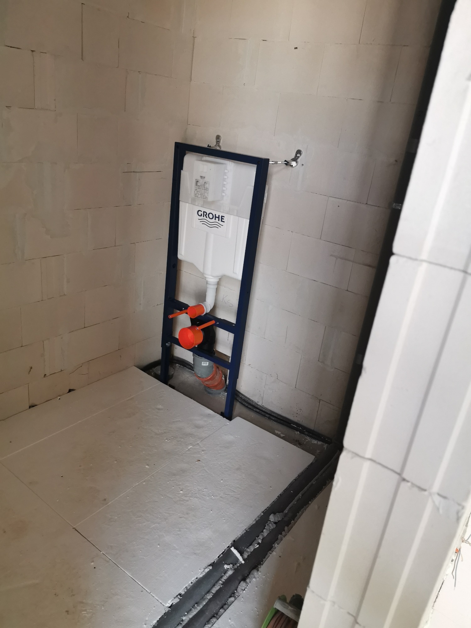 Stelaż podtynkowy WC marki Grohe zamontowany w surowym wnętrzu łazienki z bloczków, widoczne elementy instalacji hydraulicznej i kanalizacyjnej.