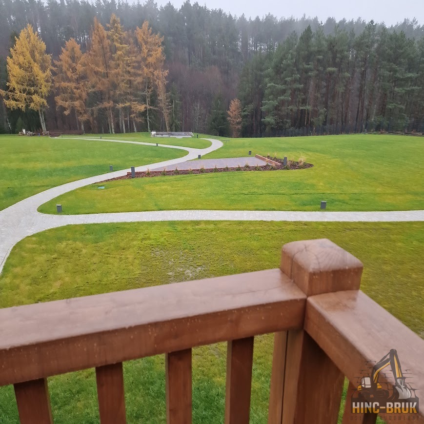 Ścieżka z kostki brukowej wijąca się przez trawnik w Chełmży. Widok z balkonu na starannie ułożoną nawierzchnię i otaczającą zieleń.