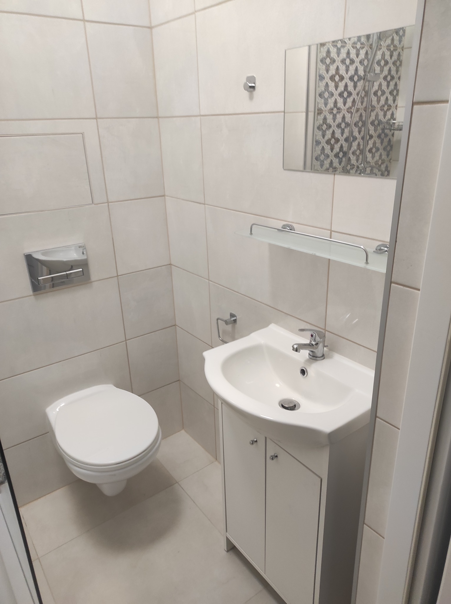 Biała umywalka z szafką, toaleta i lustro w wykończonej łazience z jasnymi płytkami.