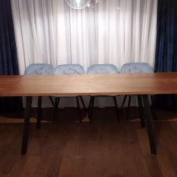 Robert Oberwan - Stół z blatem drewnianym na czarnych nogach, otoczony czterema błękitnymi krzesłami, na tle białych i granatowych zasłon, w mieszkaniu w Krakowie.