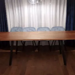 Stół z blatem drewnianym na czarnych nogach, otoczony czterema błękitnymi krzesłami, na tle białych i granatowych zasłon, w mieszkaniu w Krakowie.