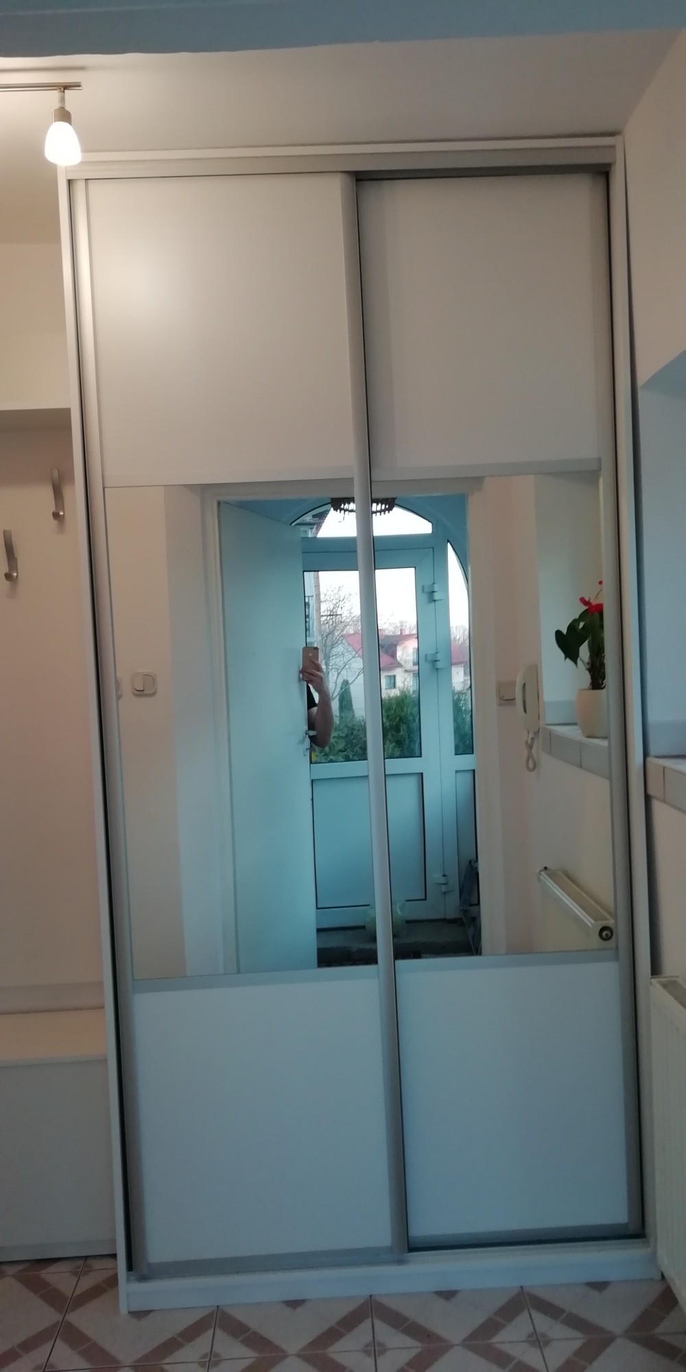 Biała szafa przesuwna z lustrem, w którym odbija się wejście do domu z widokiem na ogród