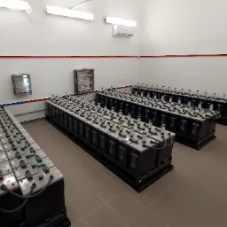 Rządowe ułożenie akumulatorów przemysłowych w serwerowni lub innym pomieszczeniu technicznym, widoczne przewody i złącza, na ścianie klimatyzator.