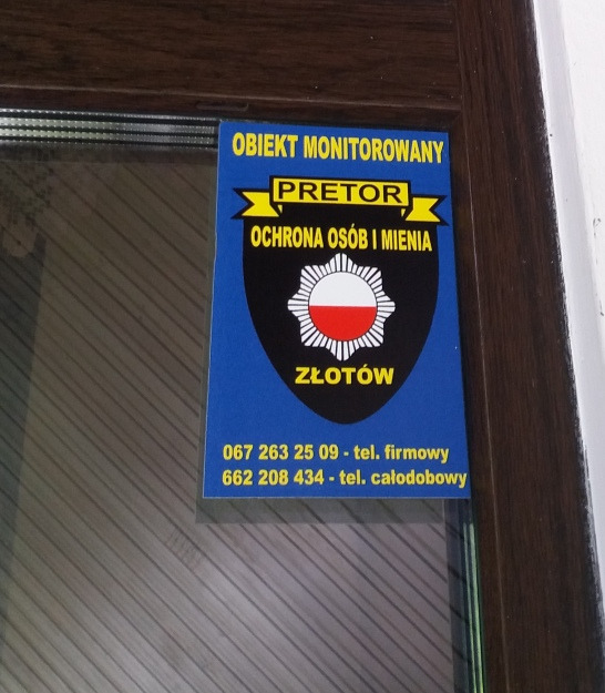 Niebieska naklejka z logo firmy ochroniarskiej Pretor na drzwiach, informująca o monitoringu obiektu w Złotowie, zawierająca numery telefonów kontaktowych.