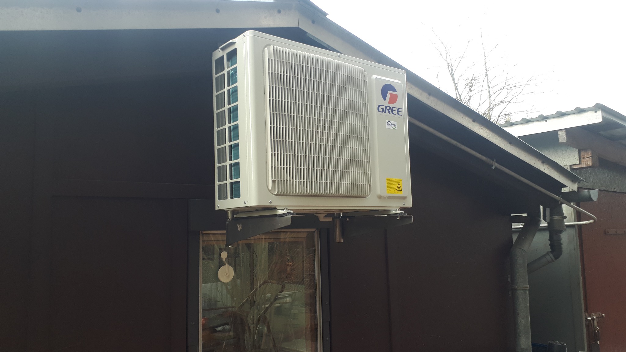 Zewnętrzna jednostka klimatyzacji GREE MUSE 3,5kW zamontowana na wspornikach nad oknem, widoczna na tle ciemnej elewacji budynku.