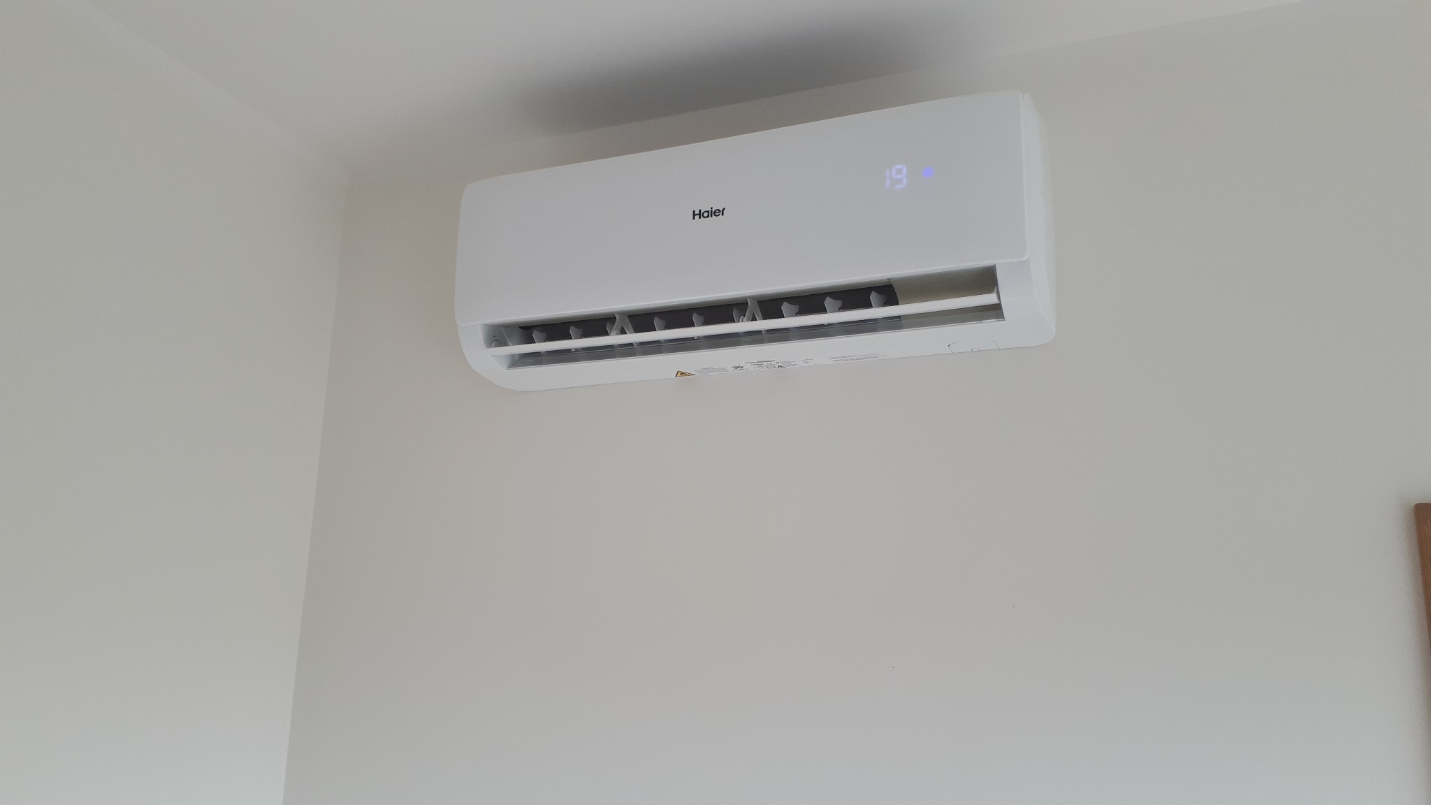 Biały klimatyzator Haier Tundra 3.5kW zamontowany na jasnej ścianie z widocznym wyświetlaczem temperatury 19 stopni Celsjusza.