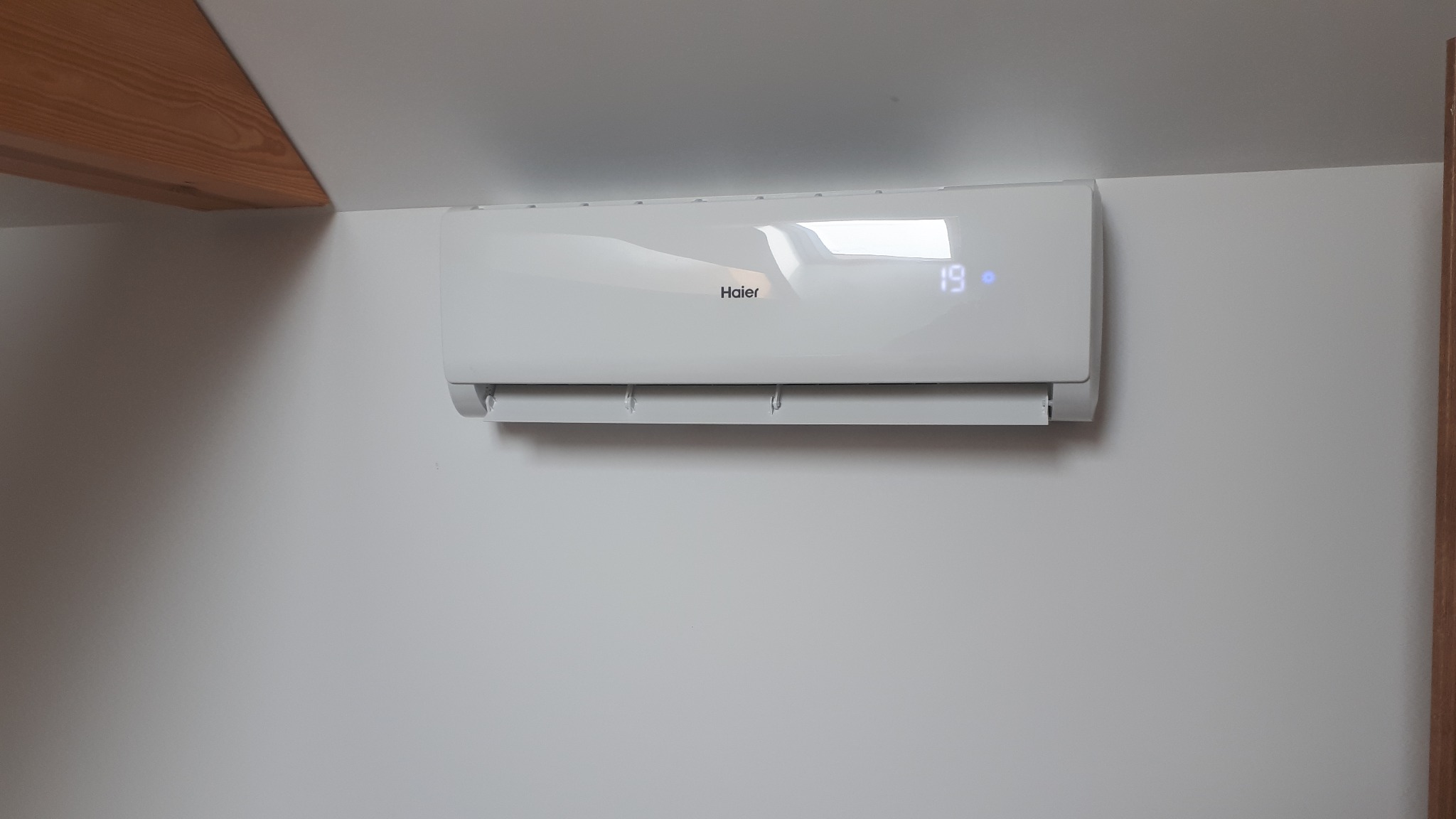 Biały klimatyzator Haier Tundra 3.5kW zamontowany na białej ścianie pod skosem sufitu, wyświetlający temperaturę 19 stopni Celsjusza.