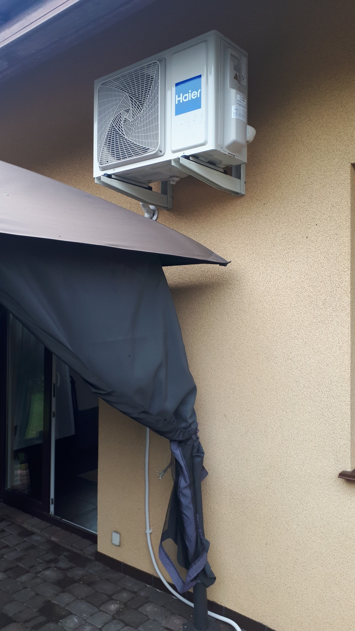 Zamontowana jednostka zewnętrzna klimatyzatora Haier na elewacji domu, widoczna zadaszona przestrzeń tarasu.