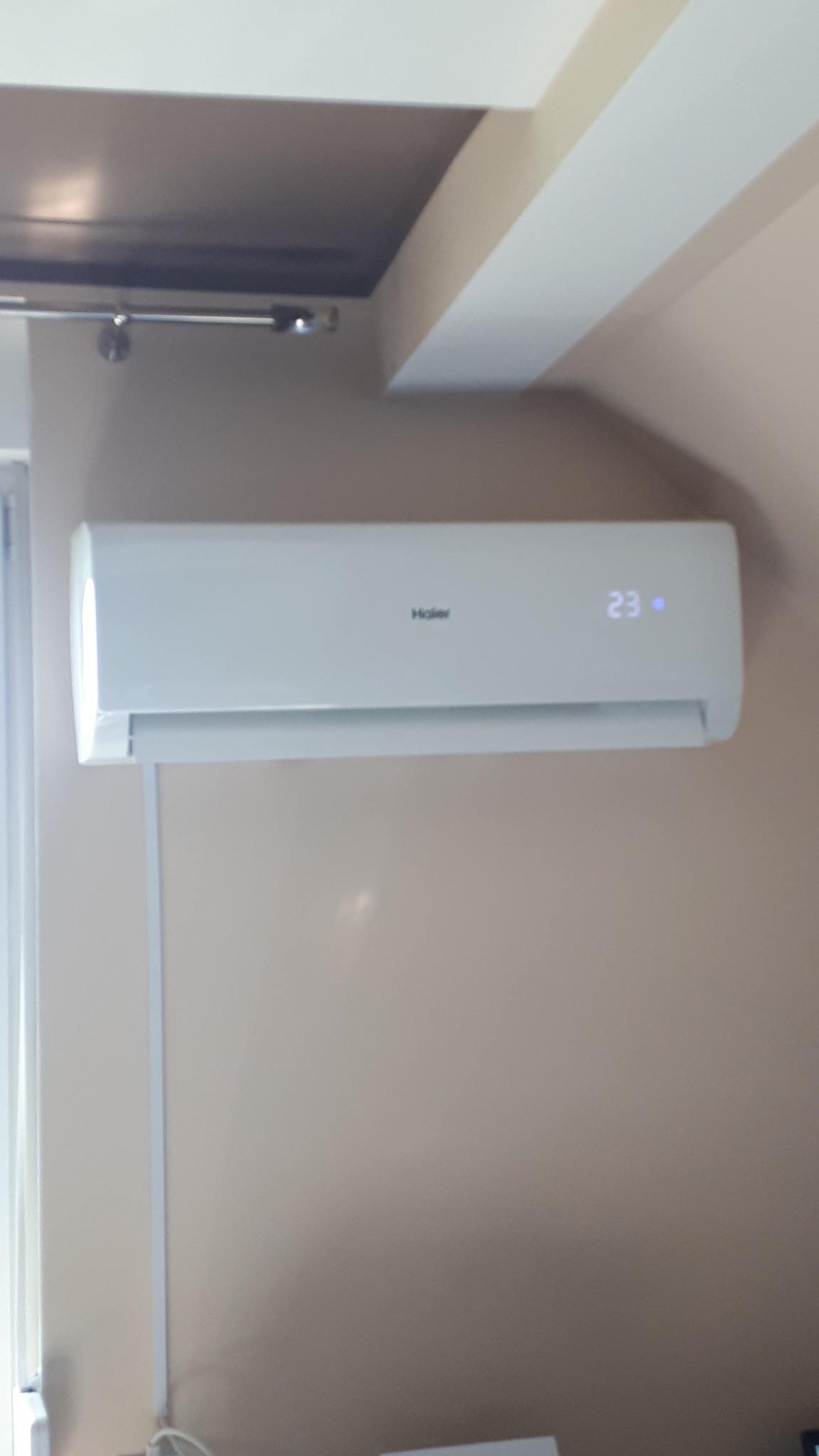 Zamontowany klimatyzator Haier Tundra z wyświetloną temperaturą 23 stopnie Celsjusza, widoczny na beżowej ścianie w pomieszczeniu.