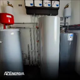 Instalacja z dwoma zbiornikami akumulacyjnymi, czerwonym naczyniem wzbiorczym i szarą pompą ciepła z niebieskim wyświetlaczem, orurowanie w pomieszczeniu technicznym, logo firmy w lewym dolnym rogu.