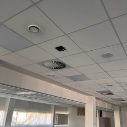 Hilow Solutions - Sufit podwieszany w biurze z widocznymi elementami wentylacji, czujnikiem dymu i okrągłymi punktami świetlnymi.