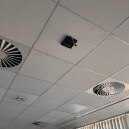 Hilow Solutions - Sufit podwieszany z kratkami wentylacyjnymi i zamontowaną czarną kamerą przemysłową z widocznym kablem.