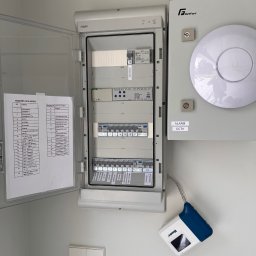 Hilow Solutions - Otwarta skrzynka elektryczna Hager z opisem obwodów, obok puszka GetFort z napisem ALARM CCTV i czujnik Hunter. Elementy instalacji inteligentnego domu.