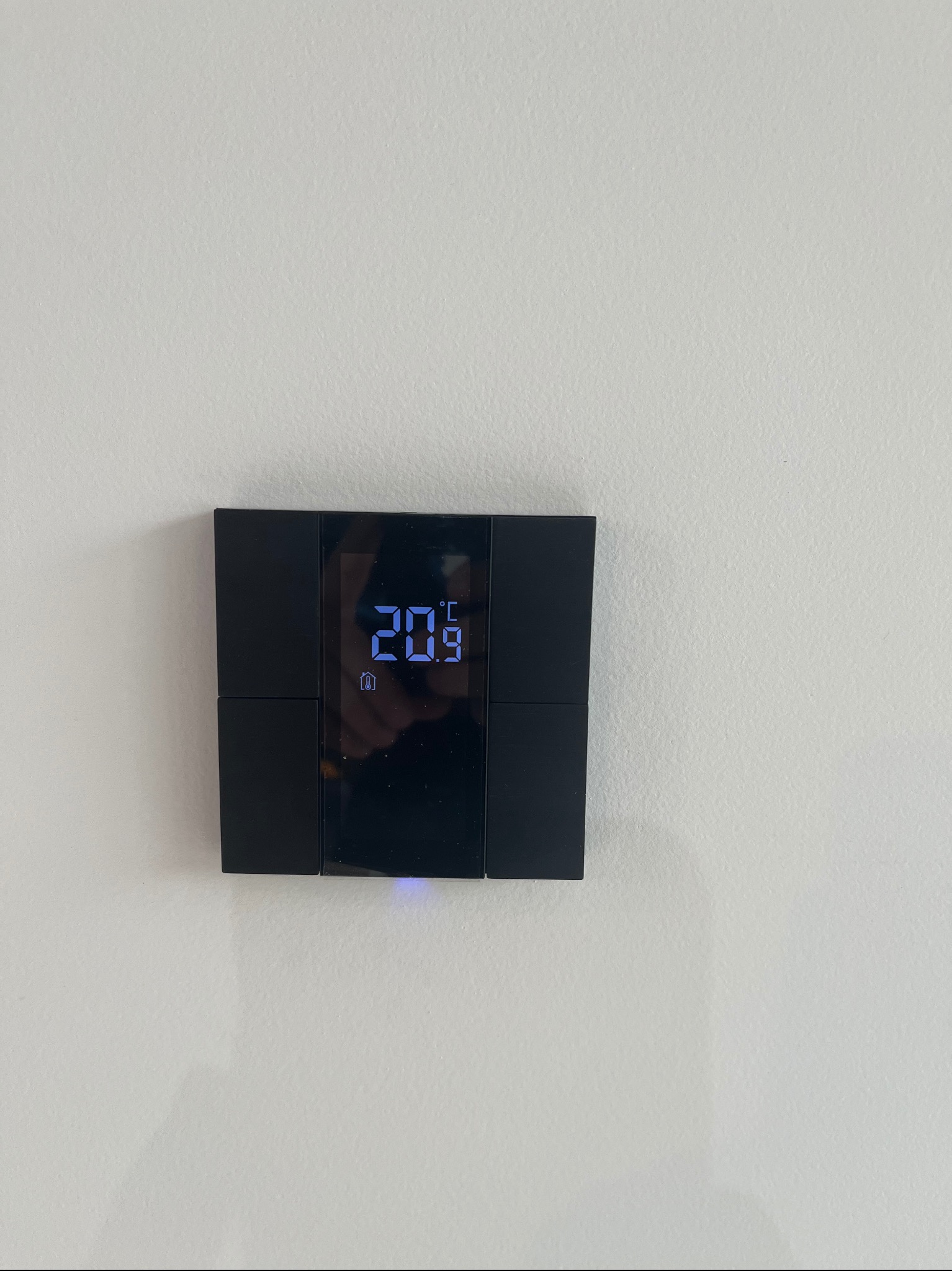 Czarny, dotykowy panel sterowania ogrzewaniem z wyświetlaczem temperatury 20.9 stopni Celsjusza, zamontowany na białej ścianie.