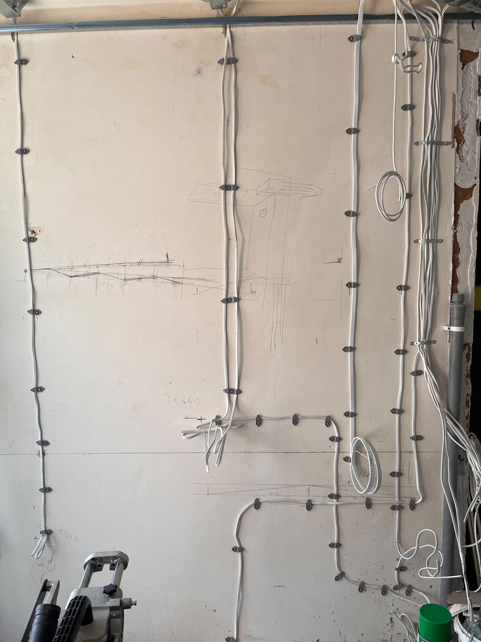 Ściana z zamocowanymi przewodami elektrycznymi, widoczne kable prowadzone wzdłuż ściany, częściowo pokrytej szkicem instalacji. Widoczne uchwyty mocujące przewody.