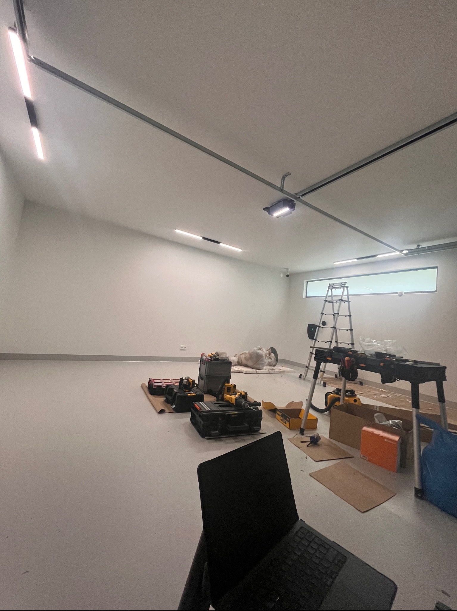 Wnętrze w trakcie montażu oświetlenia: widoczne narzędzia, drabina, lampy sufitowe i laptop. Przygotowania do instalacji elektrycznej w nowym pomieszczeniu.