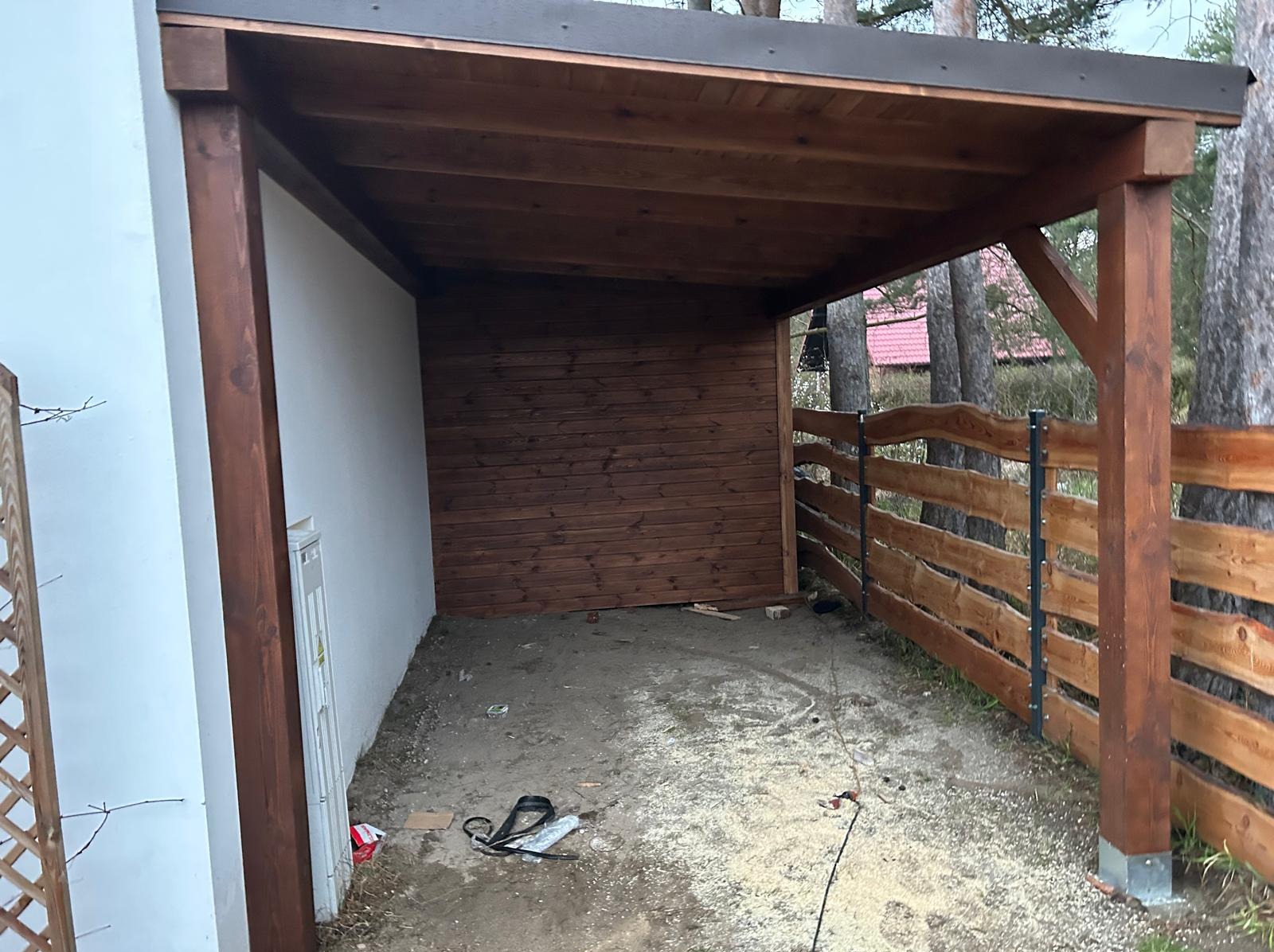 Drewniana konstrukcja z zadaszeniem, częściowo obudowana deskami, z widocznym ogrodzeniem z surowego drewna i narzędziami na ziemi. Budowa w toku.