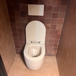 Domi-Bud - Nowoczesna toaleta w brązowej łazience z terakotą. Uwagę zwraca minimalistyczny design i ciepła kolorystyka wnętrza. Widok z góry na muszlę klozetową.