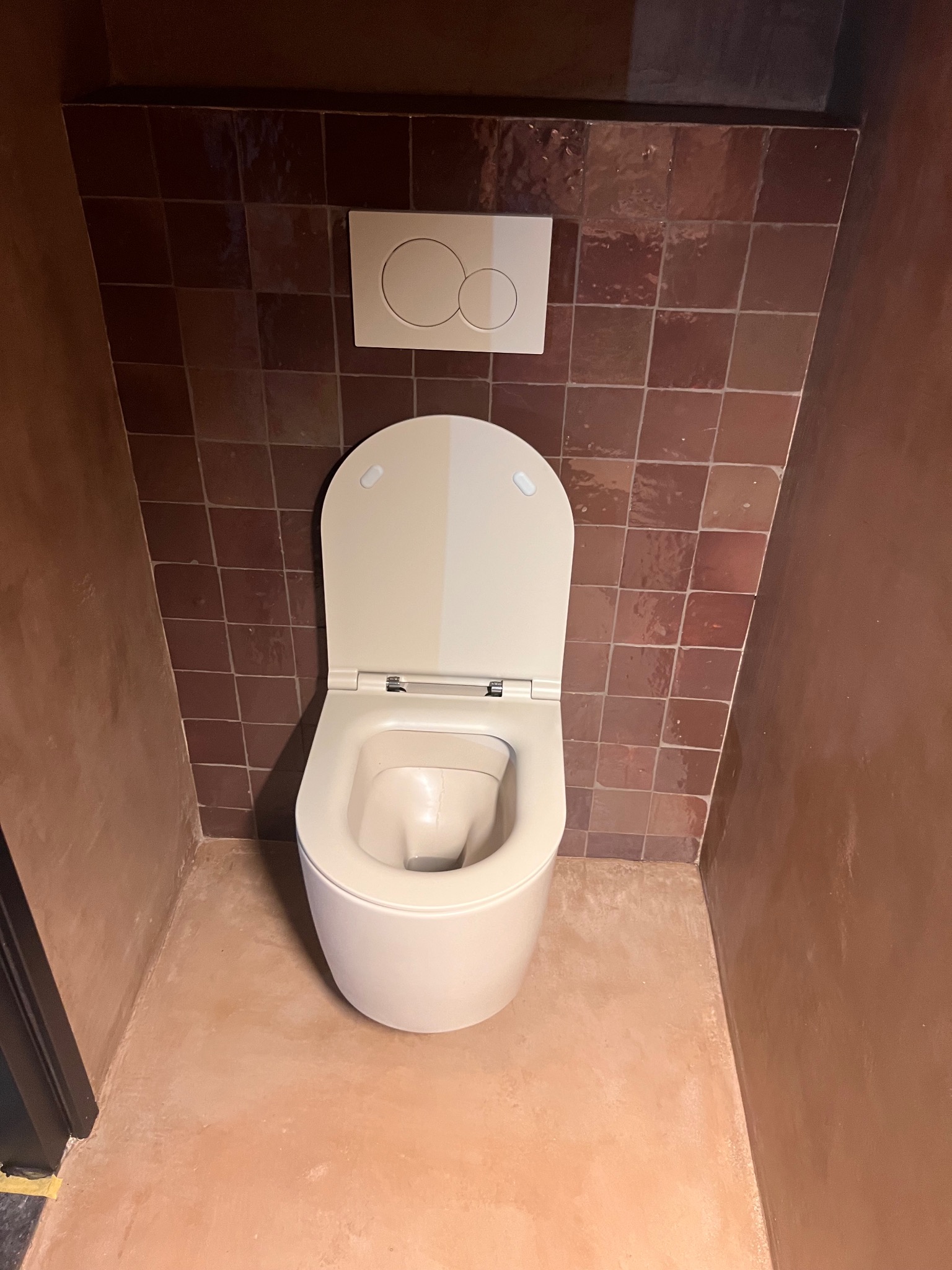 Nowoczesna toaleta w brązowej łazience z terakotą. Uwagę zwraca minimalistyczny design i ciepła kolorystyka wnętrza. Widok z góry na muszlę klozetową.