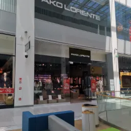 Elewacja przeszklona z widokiem na wnętrze sklepu odzieżowego Pako Lorente w galerii handlowej, widoczny napis z nazwą sklepu nad wejściem i manekiny w garniturach za szybą.