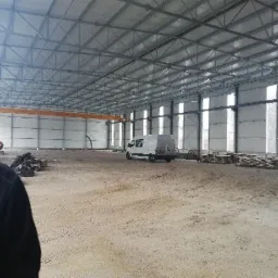 Wnętrze hali z zamontowanymi płytami warstwowymi, widoczny suwnica, palety i samochód dostawczy.