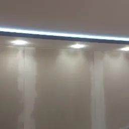 Ściana z częściowo położonymi płytami karton gips, wykończona dekoracyjnymi płytkami 3D, oświetlona punktowymi lampami sufitowymi i listwą LED w obniżonym suficie.