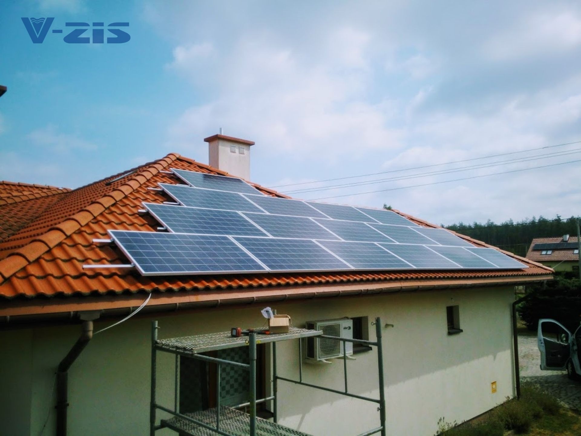 Panele słoneczne zamontowane na dachu domu z czerwoną dachówką, widoczne rusztowanie z narzędziami i klimatyzator na ścianie budynku.