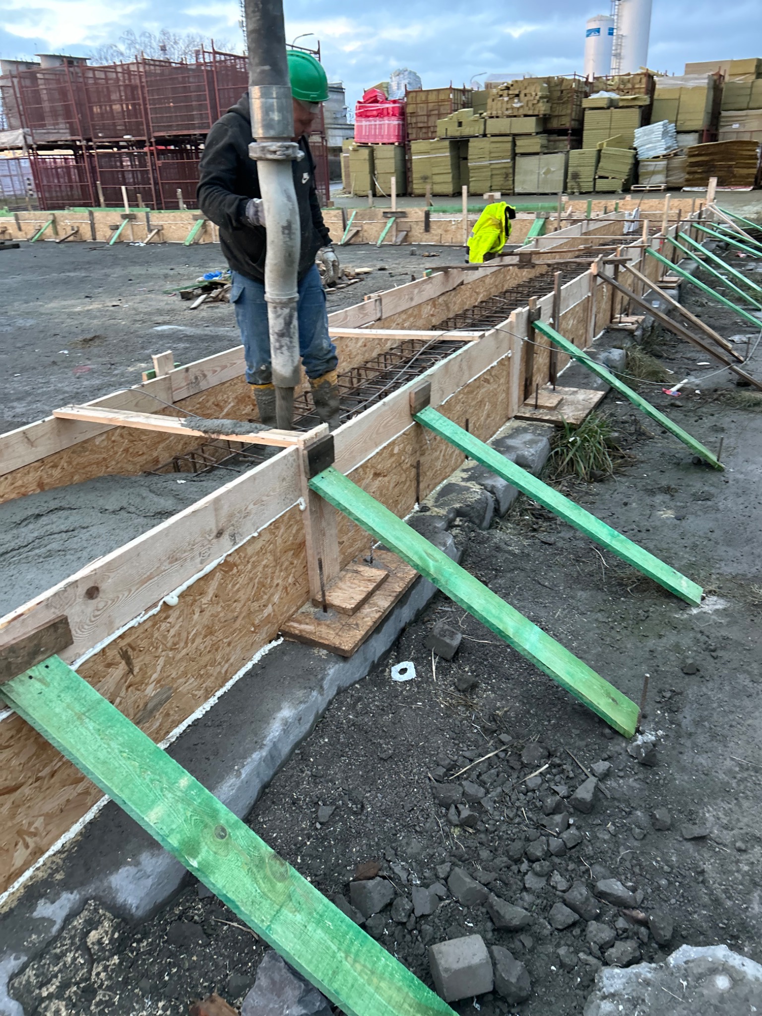 Wylewanie betonu do szalunku zbrojonego stalą; widoczne zielone podpory, betonowa pompa i pracownik w kasku.