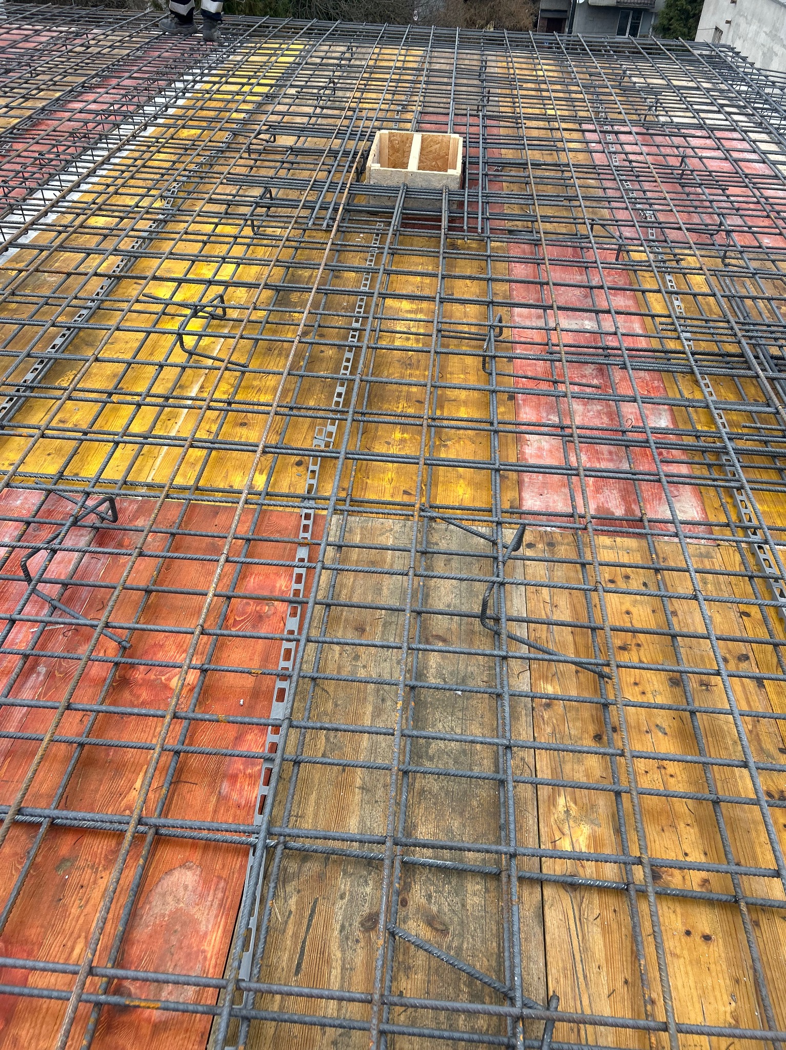 Siatka zbrojeniowa ułożona na deskowaniu z widocznymi elementami dystansowymi i otworem na instalacje, przygotowana do zalania betonem.