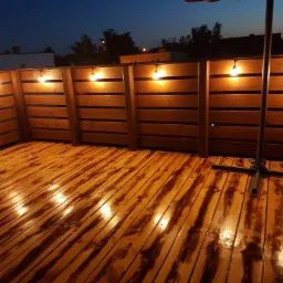 Drewniany balkon z oświetleniem punktowym w ciepłych barwach, widok po zmroku, widoczna konstrukcja parasola.