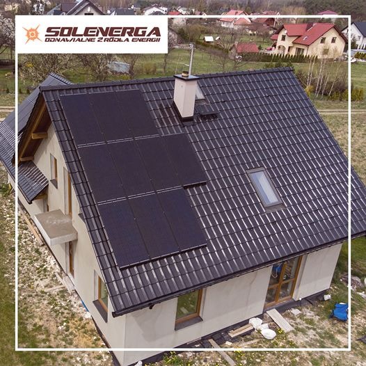 Cztery panele słoneczne, zamontowane na dachu domu z ciemną dachówką, widoczne z lotu ptaka, z logo firmy Solenerga w lewym górnym rogu.