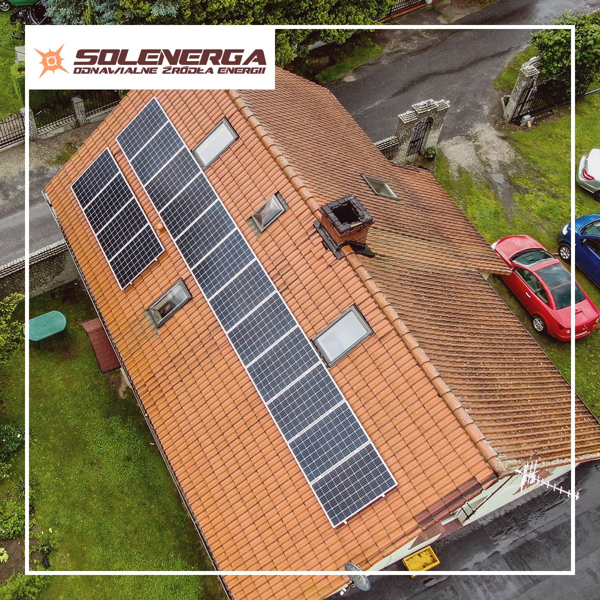 Instalacja fotowoltaiczna na dachu domu w Rydułtowach, widok z góry, z widocznymi panelami słonecznymi, kominem, oknami dachowymi i dwoma samochodami zaparkowanymi obok.