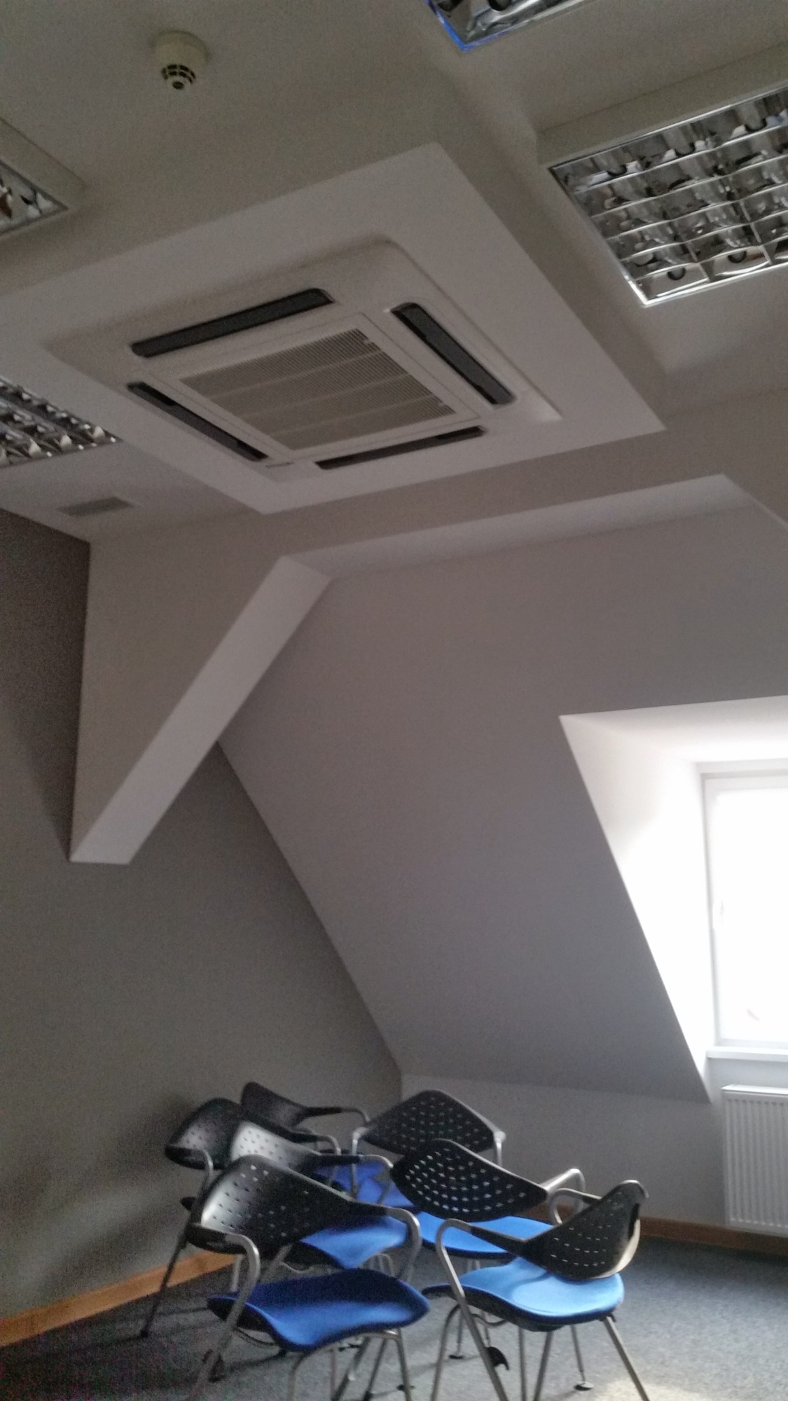 Kasetonowe urządzenie sufitowe z czarnymi elementami w biurze z krzesłami i oknem.