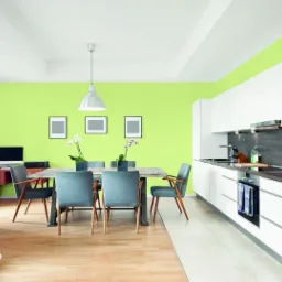 Jasnozielone ściany w nowoczesnym wnętrzu z drewnianą podłogą, szarym narożnikiem, stołem jadalnym z szarymi krzesłami i białymi meblami kuchennymi.