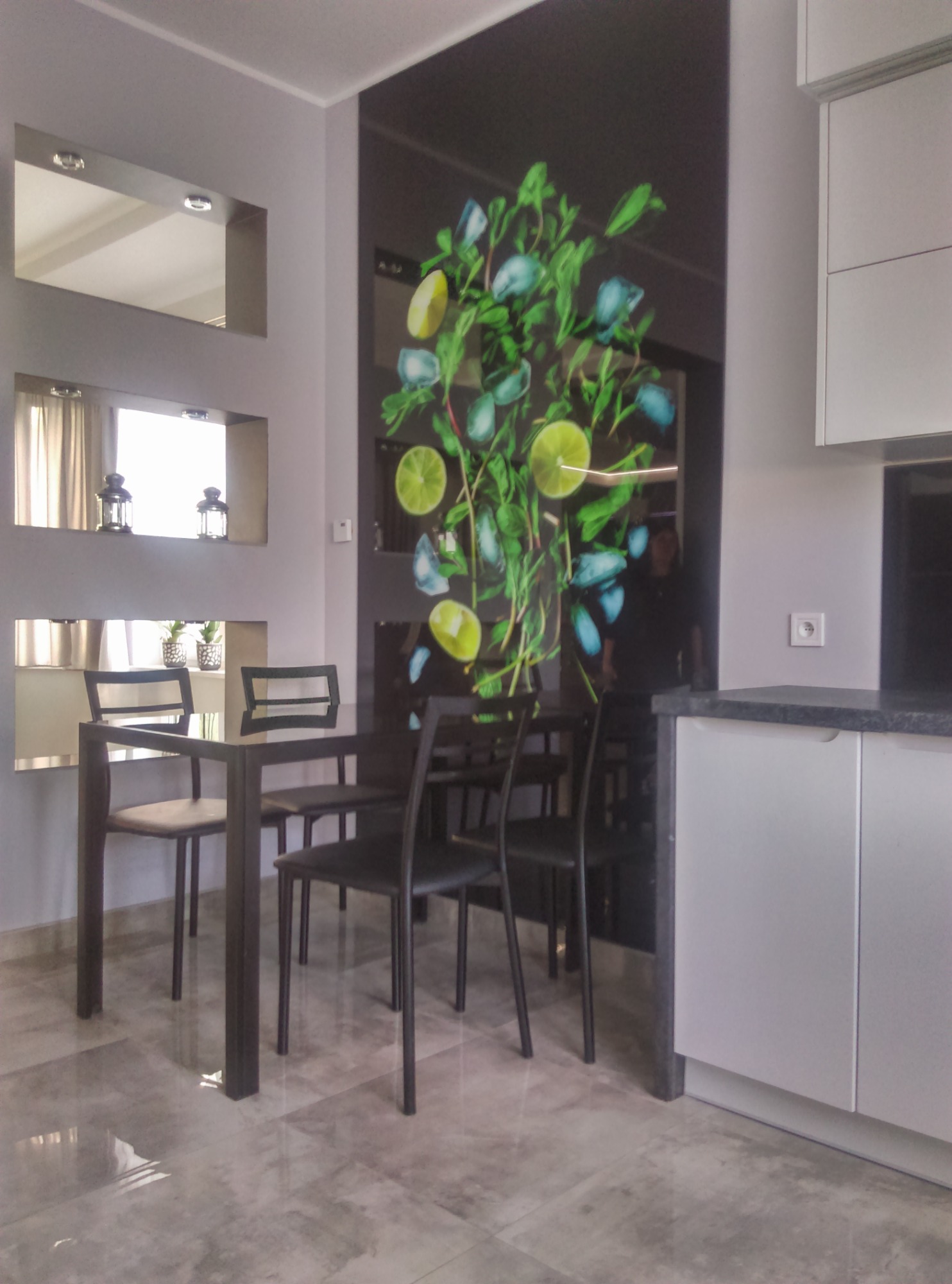 Jadalnia z ciemnym stołem i krzesłami, szarymi ścianami z wnękami i lustrami oraz panelem dekoracyjnym z motywem cytryn i mięty.