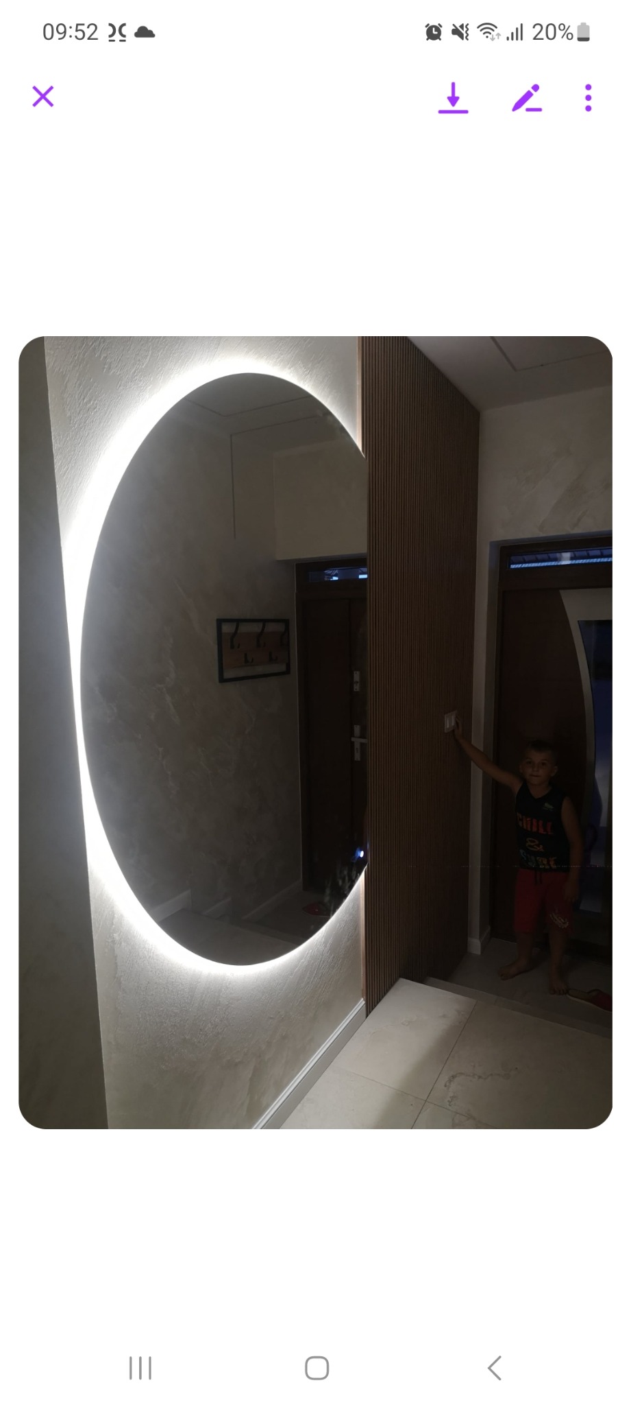 Nowoczesne wykończenie przedpokoju w Tomaszowie Mazowieckim z okrągłym lustrem z podświetleniem LED, drewnianą ścianką działową z listew i dekoracyjnym tynkiem na ścianie. Chłopiec w tle włącza...