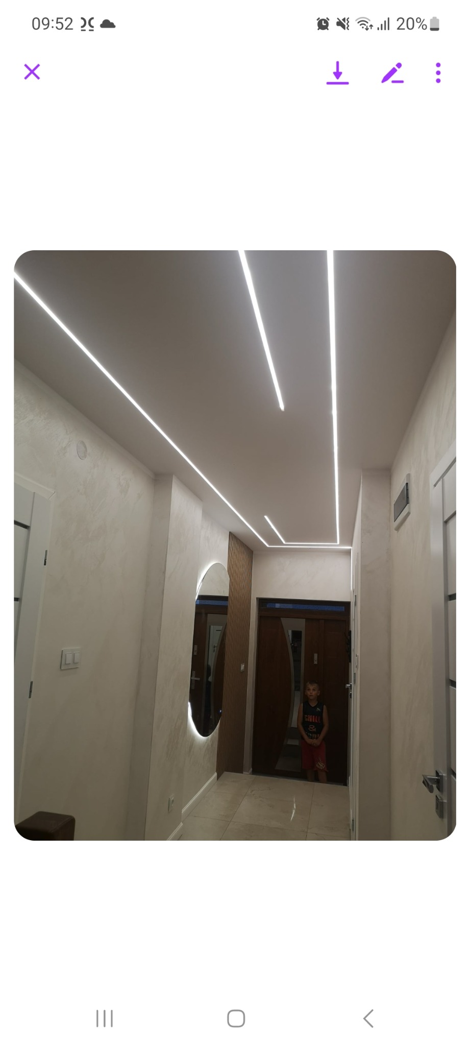 Korytarz z nowoczesnym oświetleniem LED w postaci linii na suficie, ozdobnym lustrem z podświetleniem i dekoracyjną ścianą z drewnianymi panelami.