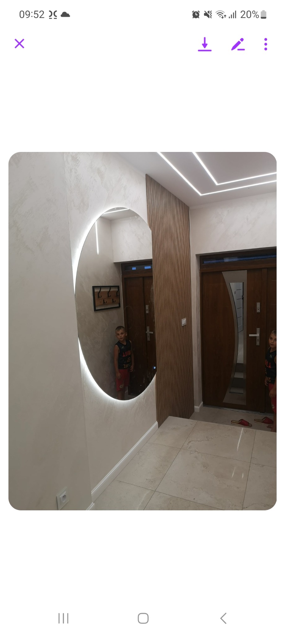 Nowoczesny przedpokój z okrągłym lustrem z podświetleniem LED, drewnianą ścianką działową i marmurową podłogą, odbicie dziecka w lustrze.