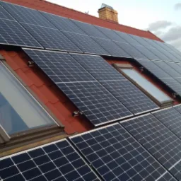 Panele słoneczne zamontowane na czerwonym dachu domu jednorodzinnego z trzema oknami dachowymi; widok z dołu pod kątem.