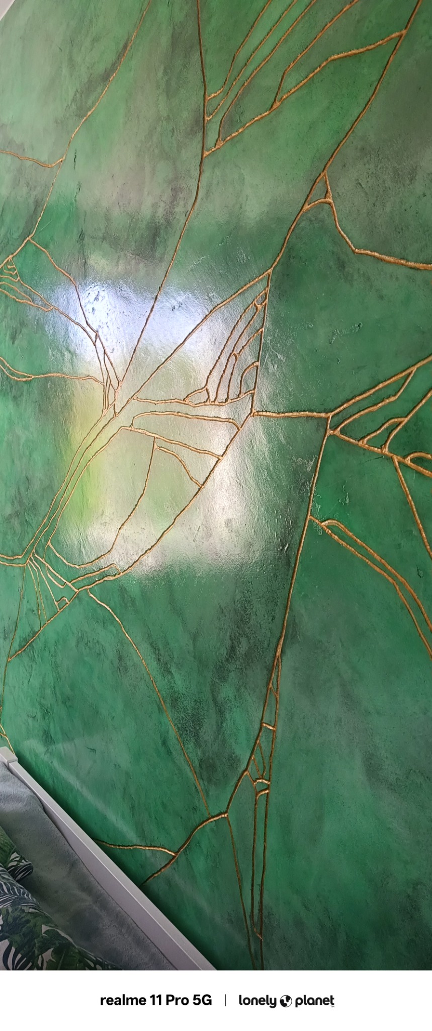 Dekoracyjna ściana w odcieniach zieleni z geometrycznym wzorem w kolorze złota, wykonana techniką strukturalną, imitująca naturalne spękania.