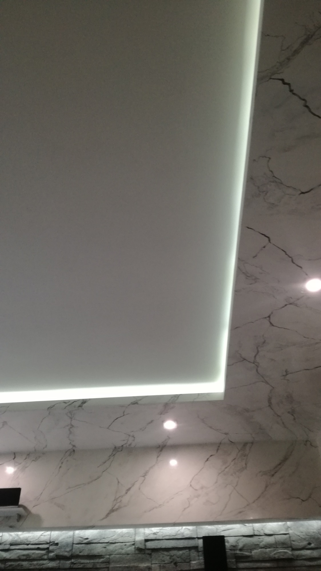 Sufit podwieszany z oświetleniem LED i ściana wykończona płytami imitującymi marmur w Złotowie.