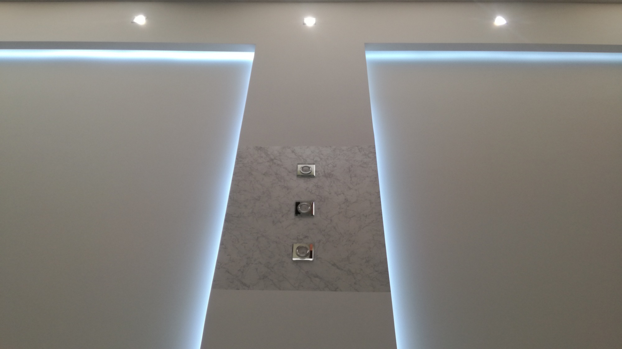 Nowoczesny sufit z podświetleniem LED po bokach i panelem dekoracyjnym imitującym marmur z trzema punktami oświetleniowymi.