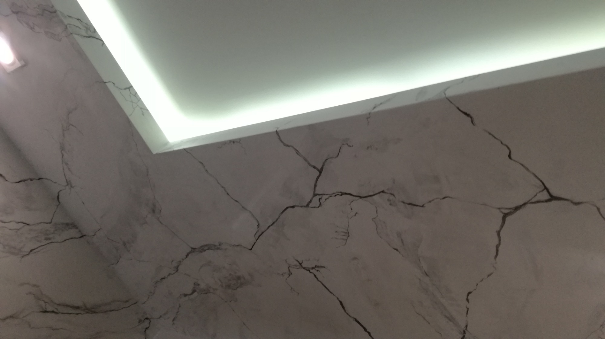 Ściana i sufit z dekoracyjną fakturą imitującą marmur z czarnymi żyłkami, oświetlenie LED w suficie podwieszanym.