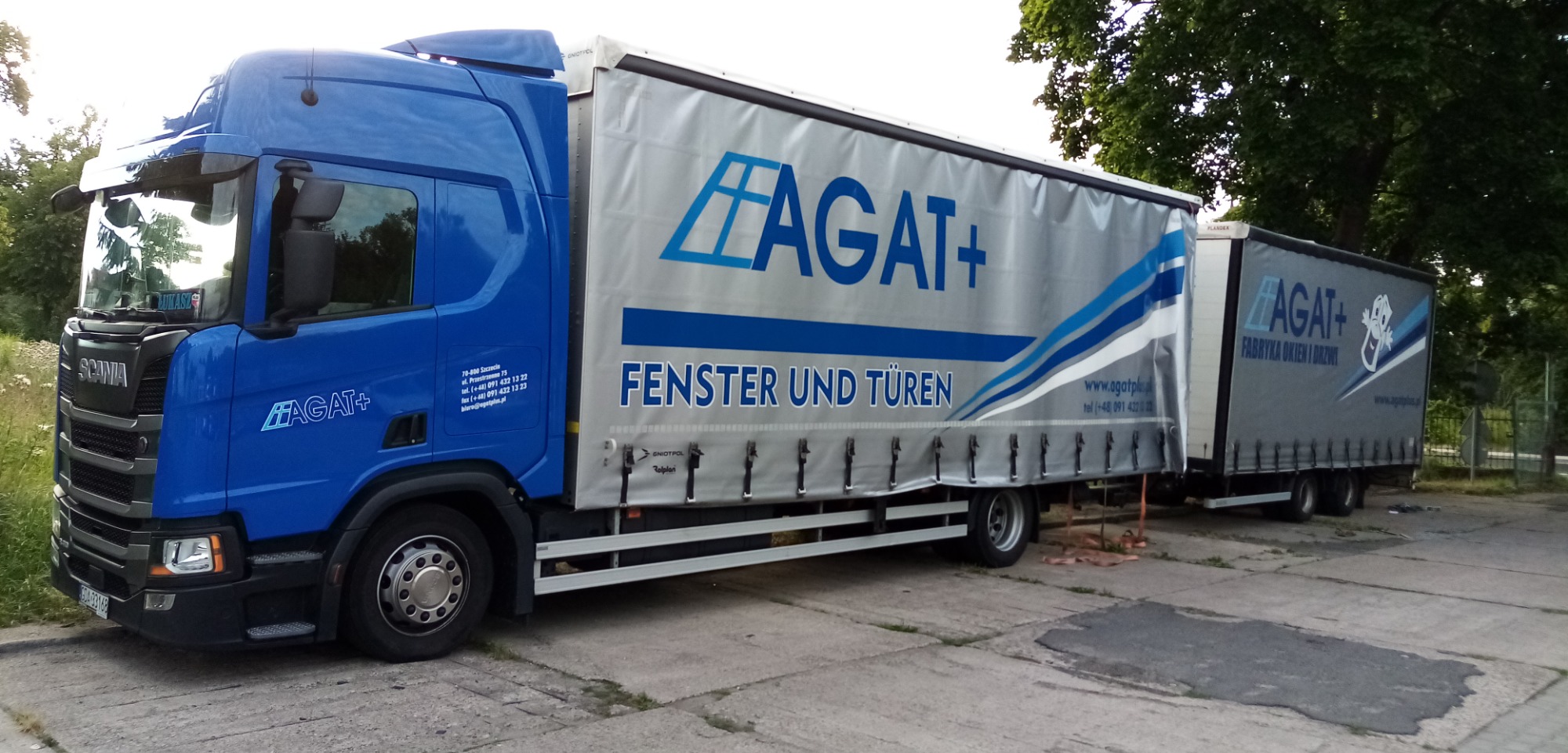 Ciężarówka firmy Agatplus z reklamą okien i drzwi, zaparkowana na betonowym placu.