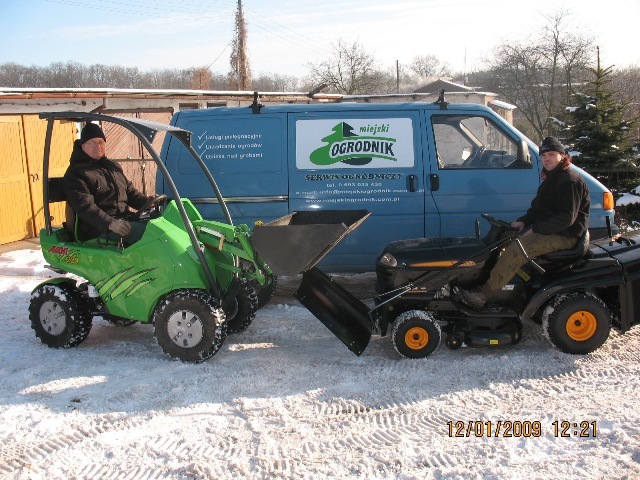 Dwaj mężczyźni siedzą na traktorach do pielęgnacji ogrodów na śniegu przed błękitnym busem z logo firmy ogrodniczej 'Miejski Ogrodnik'.